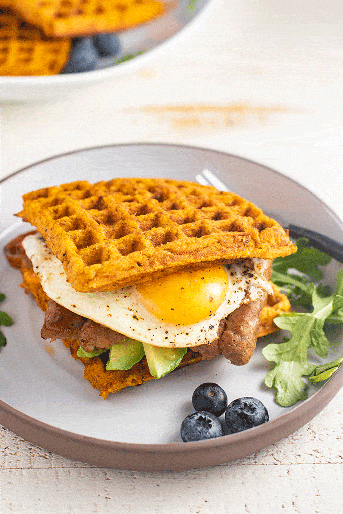 A plate with a sweet potato waffle breakfast sandwich and blueberries.