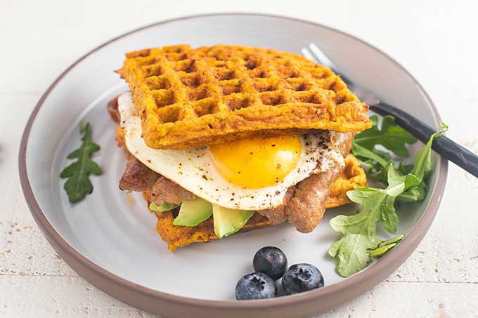 A white plate with a waffle sandwich and blueberries.