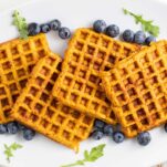 A white plate with sweet potato waffles stacked on it, surrounded by blueberries.
