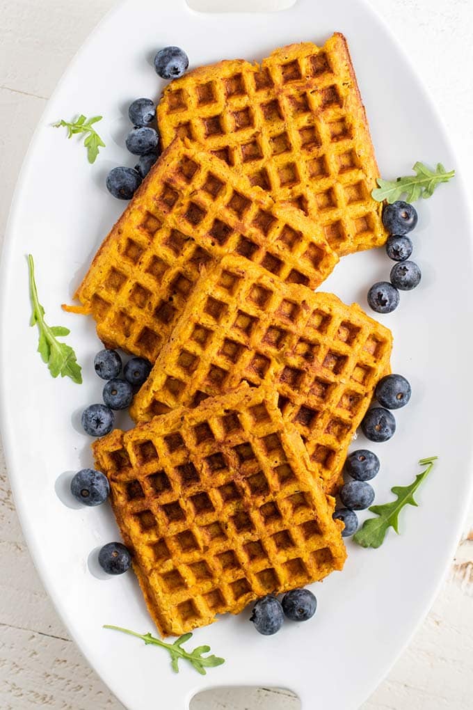 A plate with 4 sweet potato waffles, surrounded by blueberries.