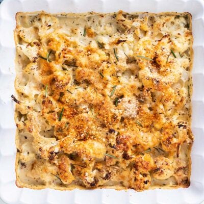A square baking dish filled with cheesy cauliflower topped with toasted breadcrumbs.