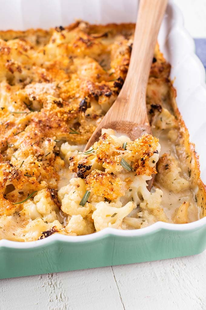 A wooden spoon scooping up a serving of cauliflower covered in cheese and toasted breadcrumbs.