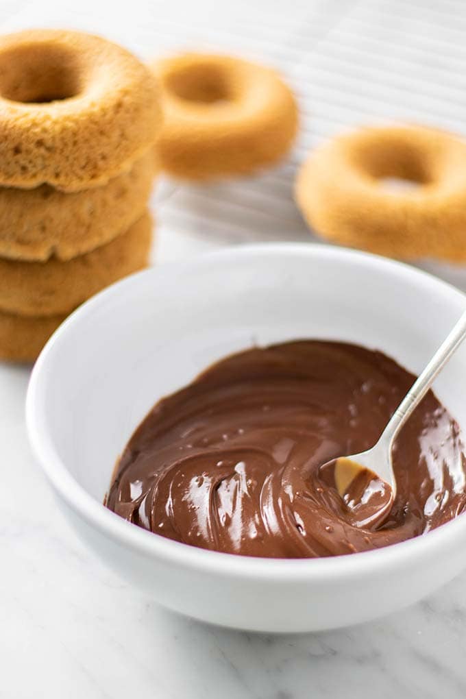 A bowl of chocolate glaze with donuts in the background.