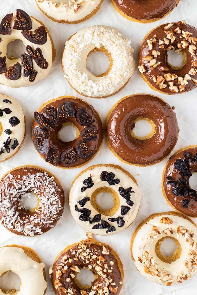 Donuts laying on white baking paper, glazed and decorated with fruit and nuts.