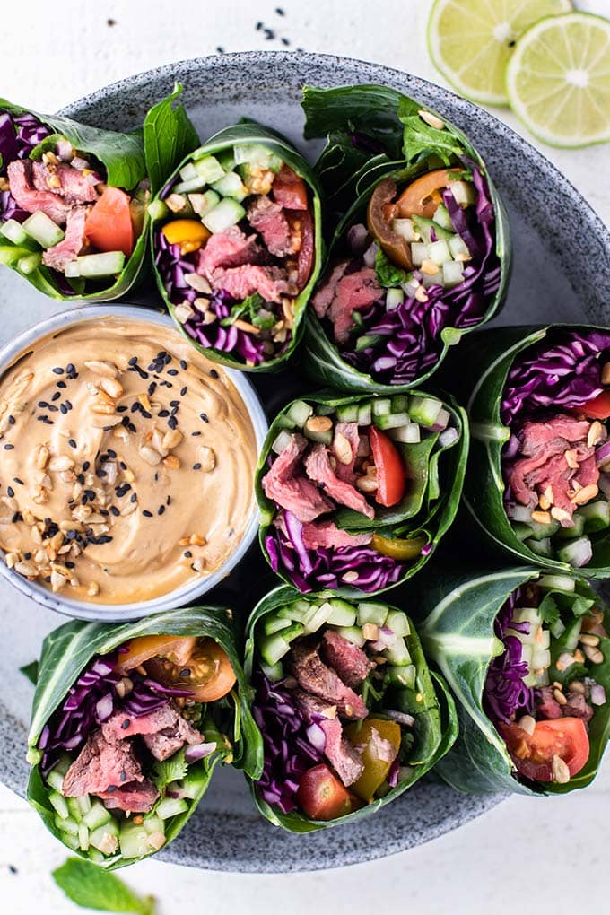 A top down close up view of collard wraps stuffed with thai steak salad on a plate with a creamy dipping sauce.