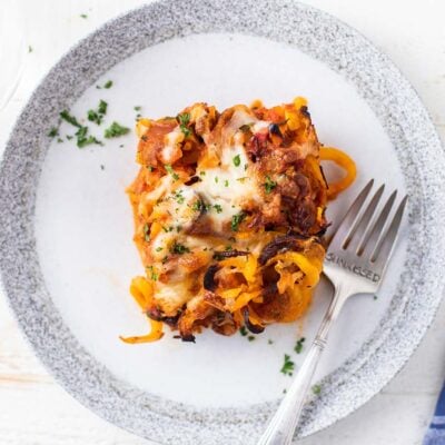 A slice of butternut squash casserole shown on a white plate with a fork.