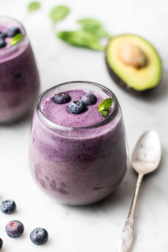 Two clear glasses filled with a blueberry green smoothie garnished with mint.