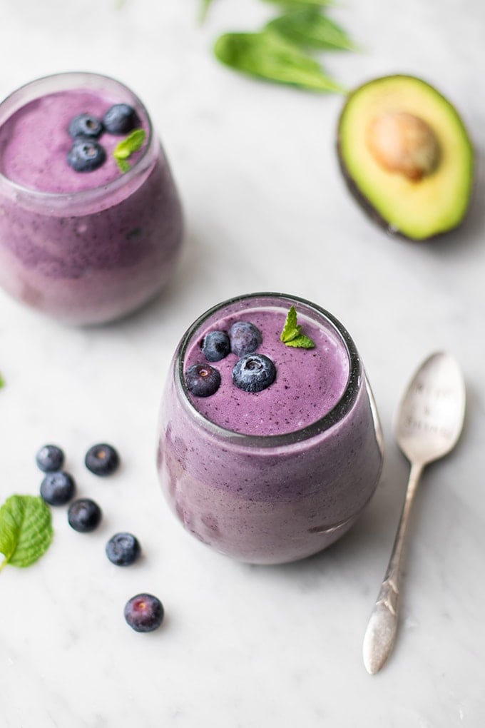 Two clear glasses filled with a blueberry green smoothie garnished with mint.