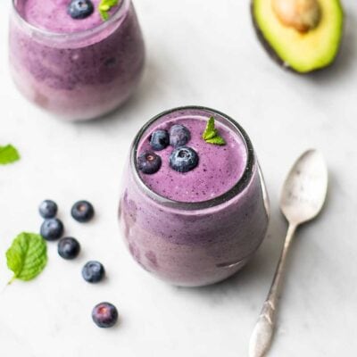 Two blueberry smoothies in clear glasses garnished with fresh blueberries.