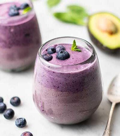 Two clear glasses filled with a blueberry green smoothie garnished with mint.