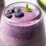 A close up of a blueberry smoothie in a clear wine glass.