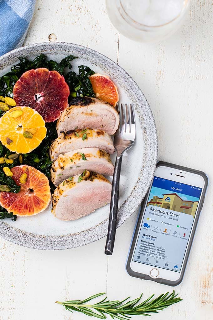 A plate shown with a kale and blood orange salad served with slices of a baked pork tenderloin.