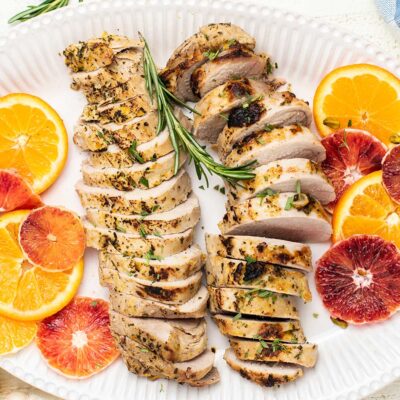 A platter with two baked pork tenderloins, sliced and served with blood oranges and mandarins.