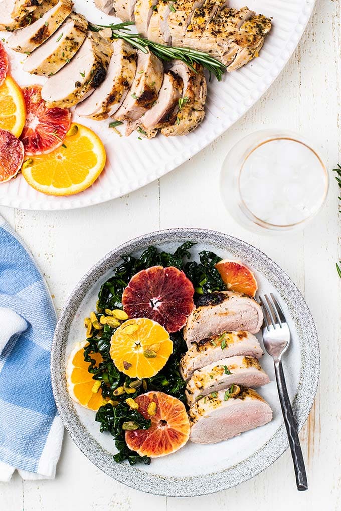 A platter with sliced pork tenderloin next to a plate with kale salad and baked pork tenderloin slices.