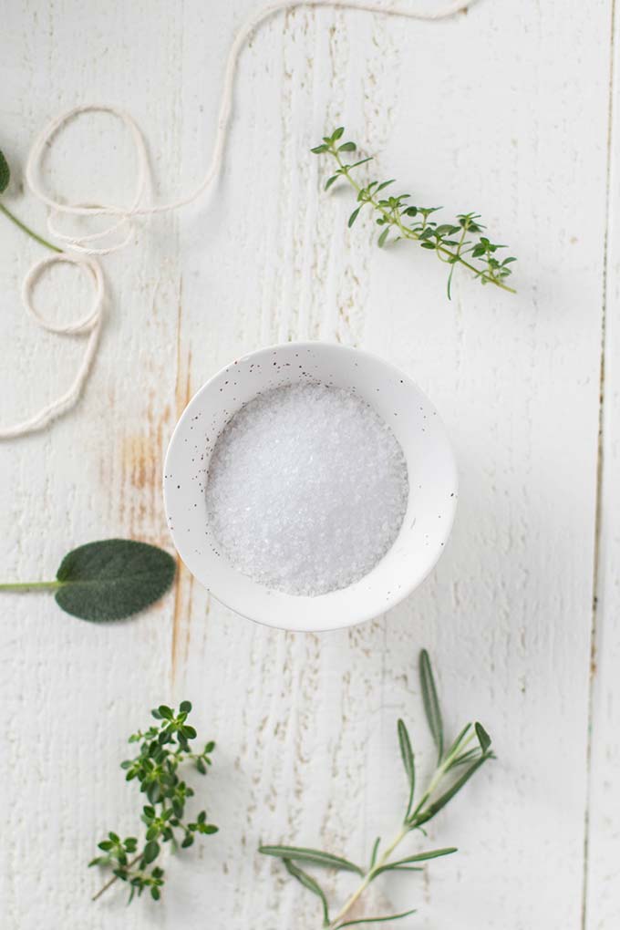 A bowl of coarse salt surrounded by sage, thyme, and rosemary.