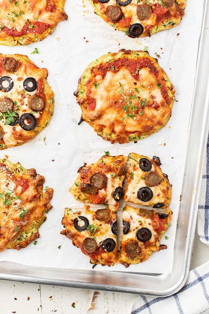 6 mini zucchini pizza crusts topped with cheese, sausage, and olives.