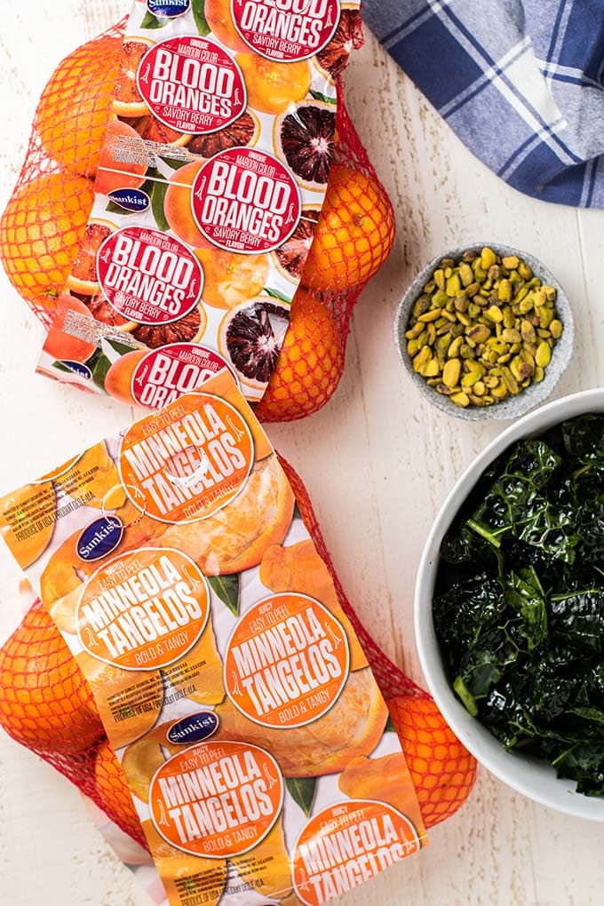 A bag of blood oranges, a bag of minneola tangerines, next to a white salad bowl full of massaged kale.