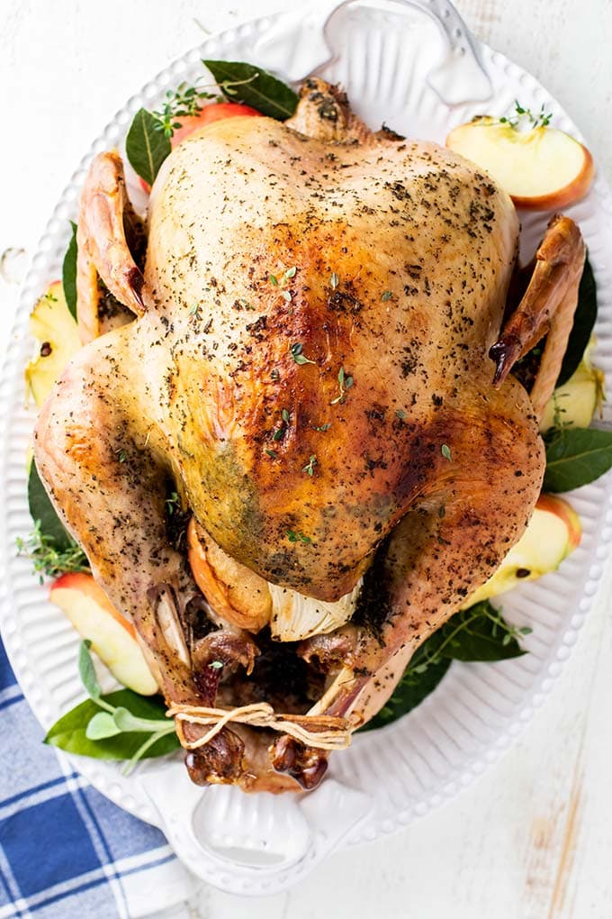 A roasted turkey on a platter with sage leaves and apples.