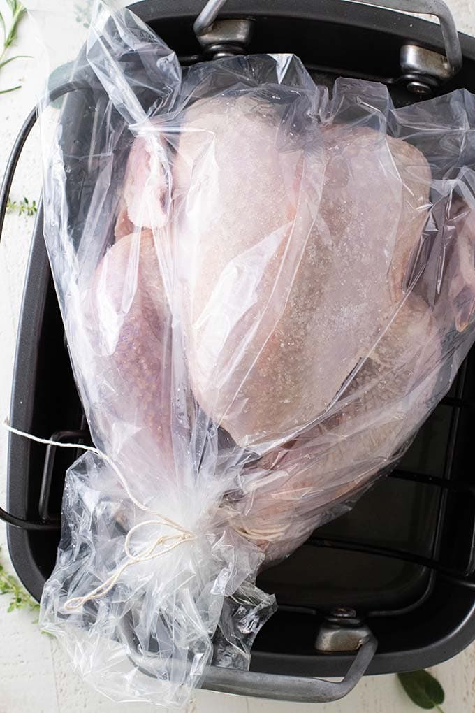 A turkey wrapped in plastic covered in coarse salt, showing how to dry brine a turkey.