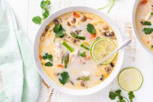 A close up look at a bowl of tom kha gai with lots of vegetables.