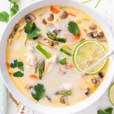 A close up look at a bowl of tom kha gai with lots of vegetables.
