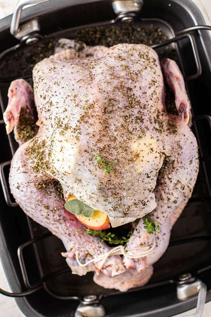 A roasting pan with an uncooked turkey coated in herbs and butter.