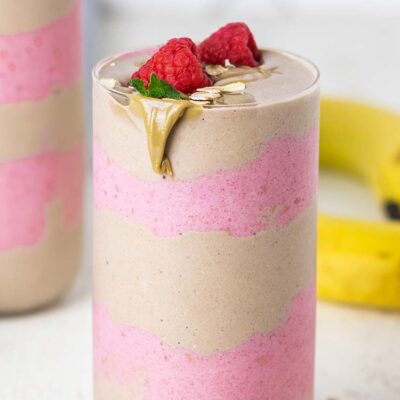 A creamy oatmeal smoothie shown in a glass with raspberry and banana layers.