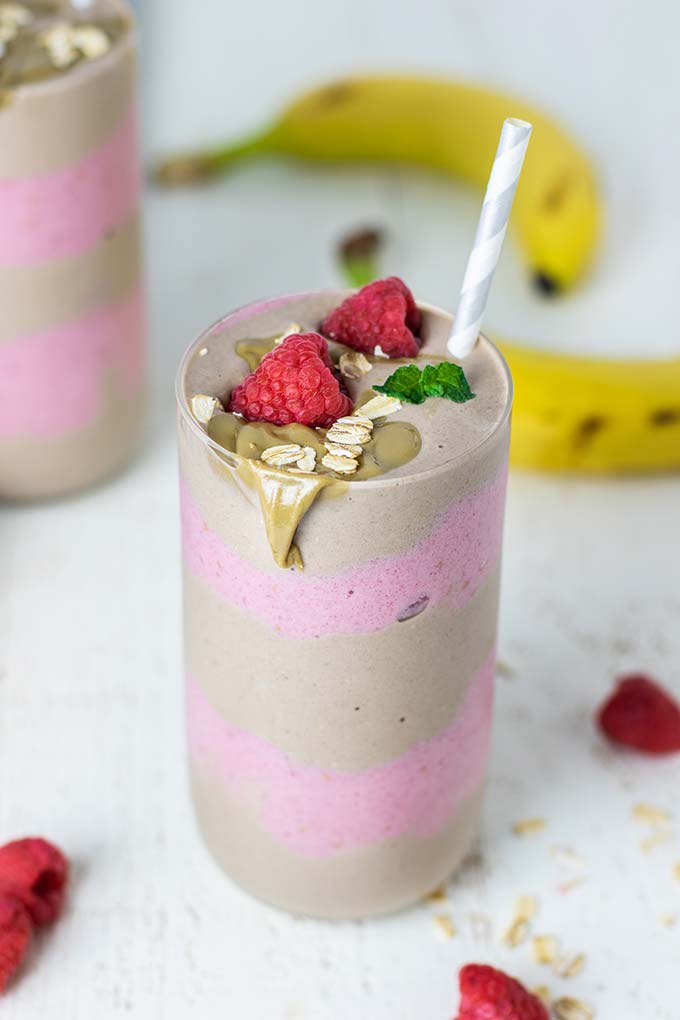 A SunButter breakfast smoothie in a glass topped with SunButter, raspberries, and oatmeal.