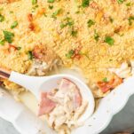 A white spoon scooping up come of the chicken cordon bleu casserole out of a baking dish.