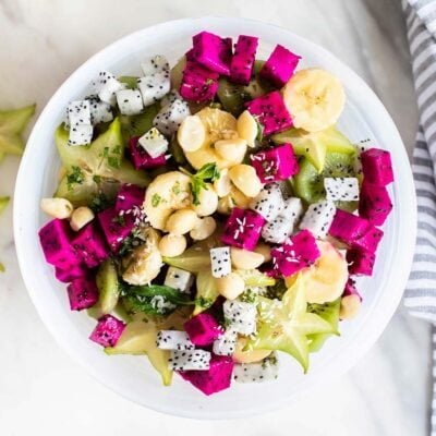 A top down view of a white bowl filled with dragon fruit, star fruit, and bananas.