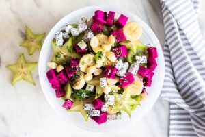 A top down view of a white bowl filled with dragon fruit, star fruit, and bananas.