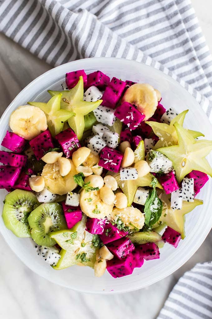 A top down view of a white bowl filled with dragon fruit, star fruit, and bananas.
