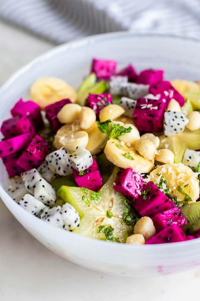 A close up side view of a dragon fruit salad topped with macadamia nuts.