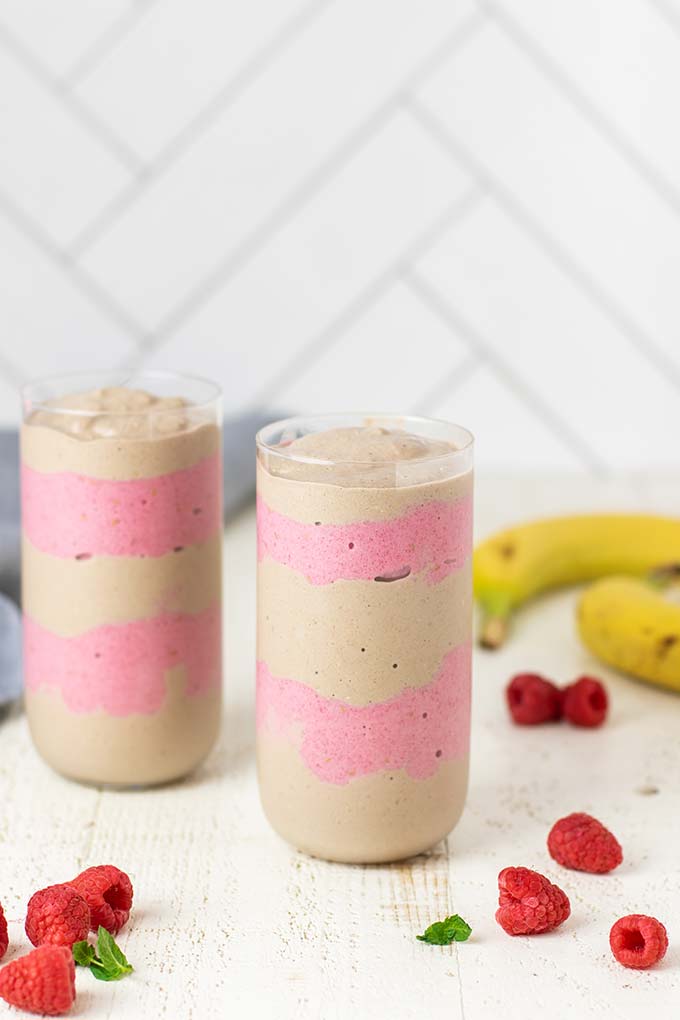 Two glasses shown with alternating layers of raspberry smoothie and sunbutter smoothie.