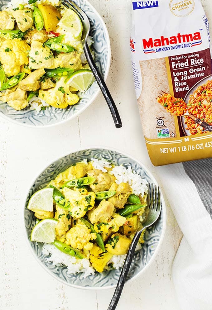 Two bowls filled with rice and a thai yellow curry, with a bag of rice.