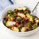 A bowl filled with crispy roasted brussels sprouts and big chunks of crisp bacon.