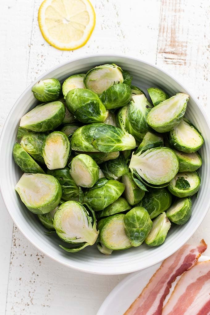 A bowl of vibrant green brussels sprouts, showing how to trim and halve them for this recipe.