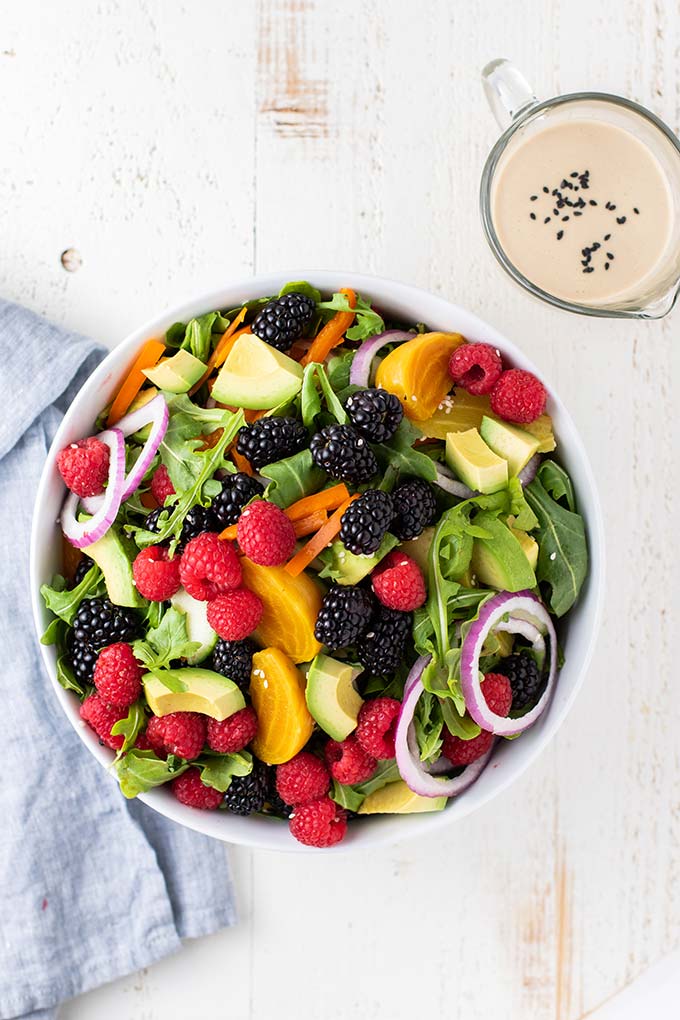 A salad bowl filled with arugula, avocado, berries, onions, and peppers.