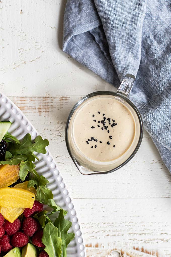 A creamy salad dressing garnished with black sesame seeds in a clear glass pour jar.