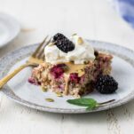 A slice of blackberry baked oatmeal on a white plate with a gold fork.