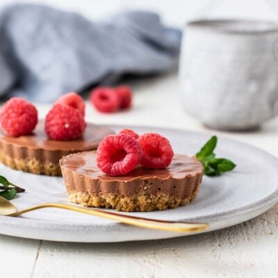 Two mini chocolate cheesecakes garnished with raspberries on a gray plate.