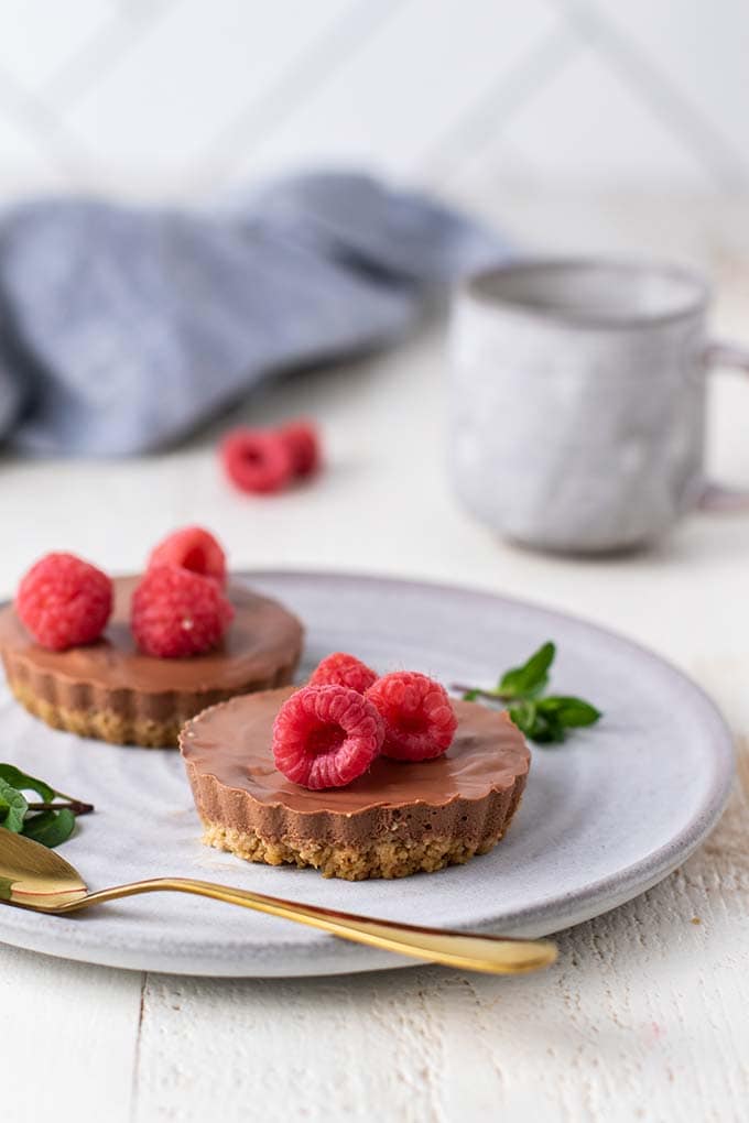 Two mini chocolate cheesecakes garnished with raspberries on a gray plate.