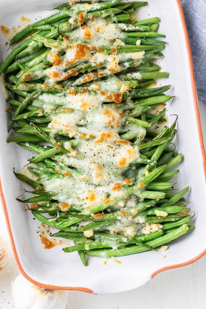 A close up look at green beans in a baking dish with a layer of browned cheese on top.
