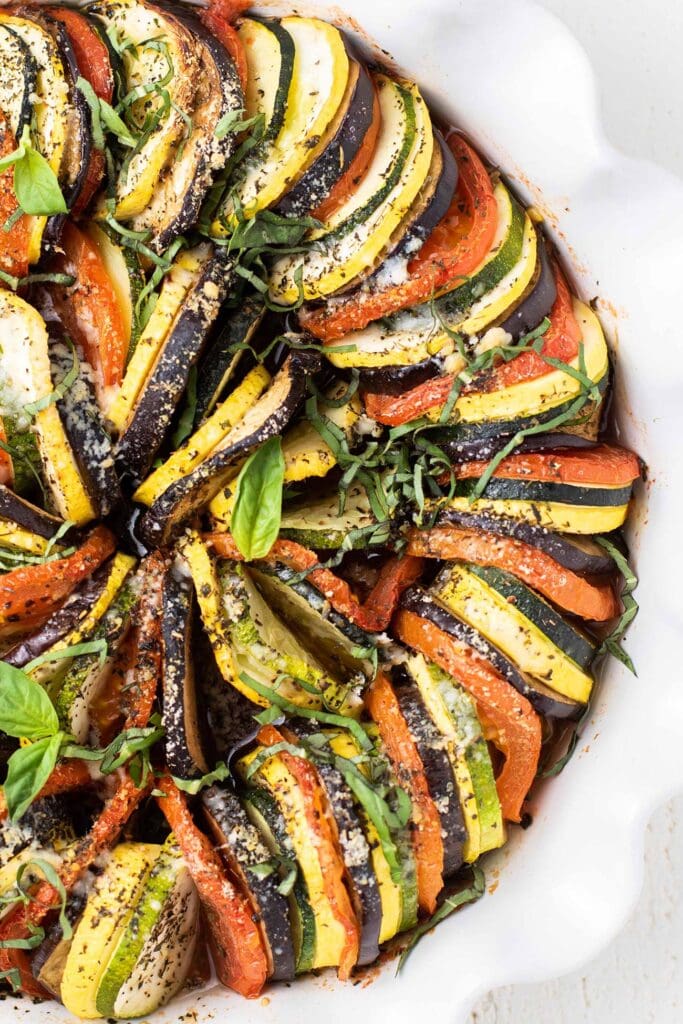 A close up look at a baked ratatouille topped with parmesan and basil.