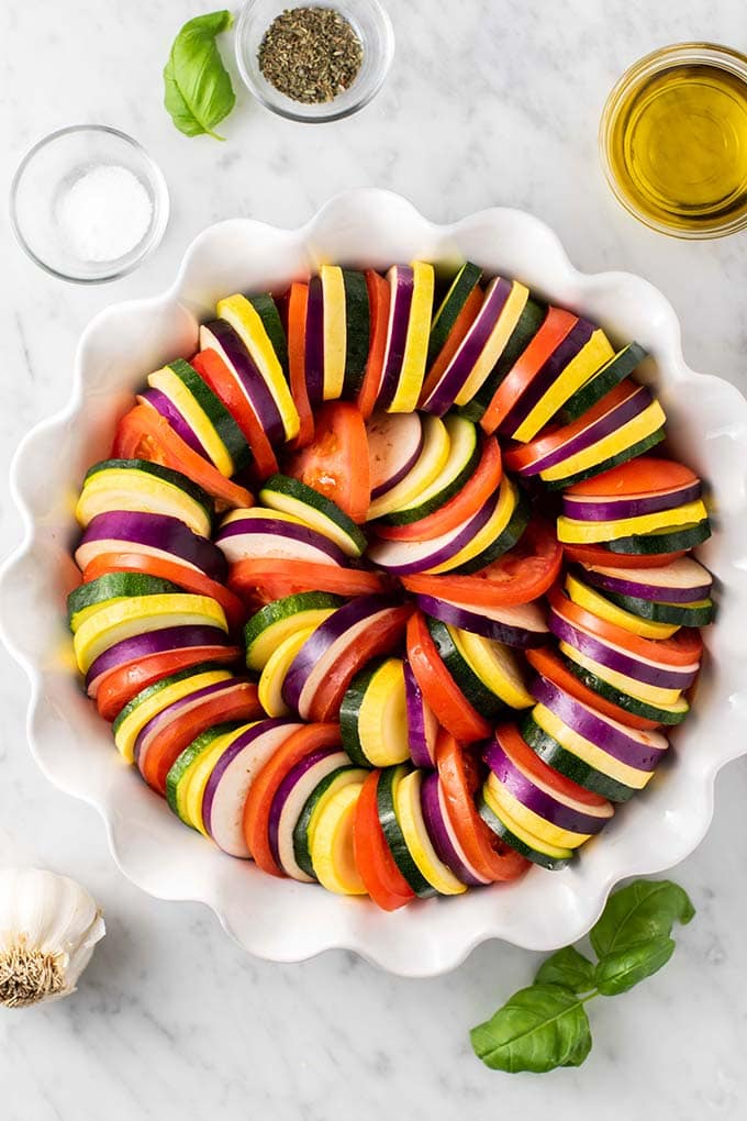 A baking dish shown with layers of tomatoes, eggplant, zucchini, and summer squash.