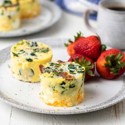 Two egg bites with kale and bacon on a plate served with strawberries.