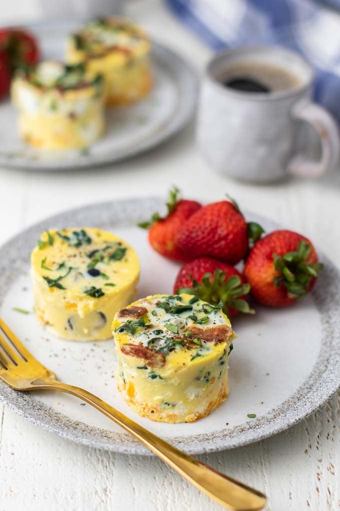 Two egg bites on a plate with strawberries next to a mug of coffee.