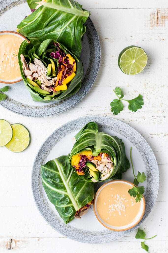 Two plates with colorful rainbow collard wraps with chicken and a creamy dipping sauce.