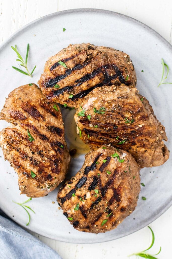 4 grilled pork chops arranged on a platter with fresh rosemary.