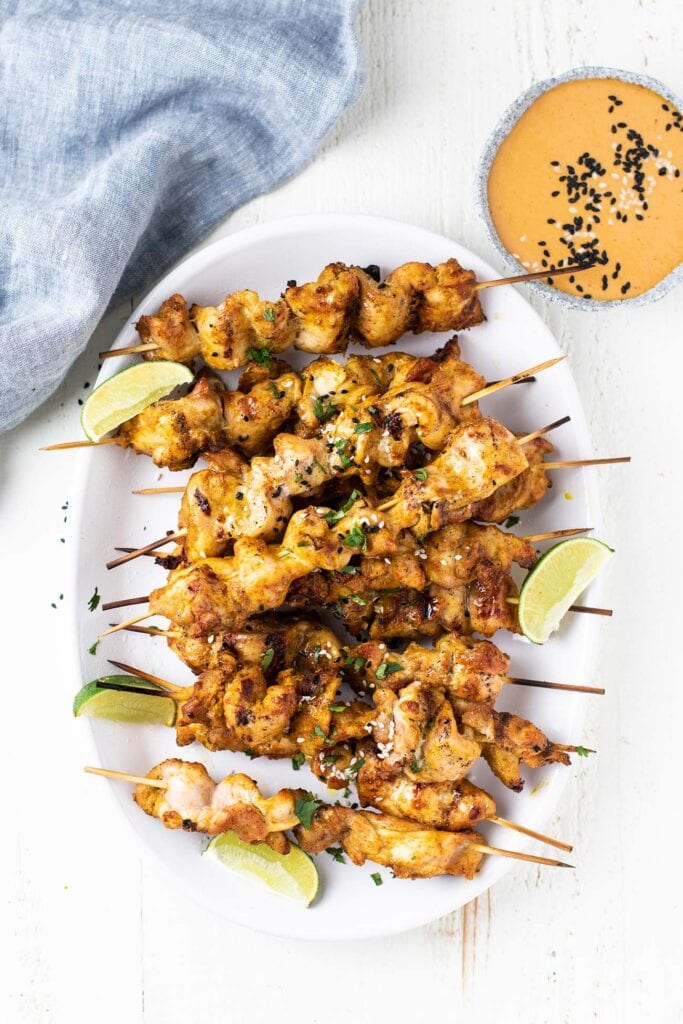 A platter with lots of grilled chicken satay skewers.